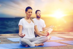 yoga and healthy lifestyle concept - people meditating in lotus pose on wooden pier over sea background